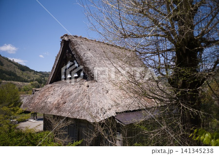 青空と山並みを背景にした合掌造りの茅葺き屋根 妻壁の装飾意匠 青空と山並みを背景にした合掌造りの茅葺き屋根 妻壁の装飾意匠 141345238