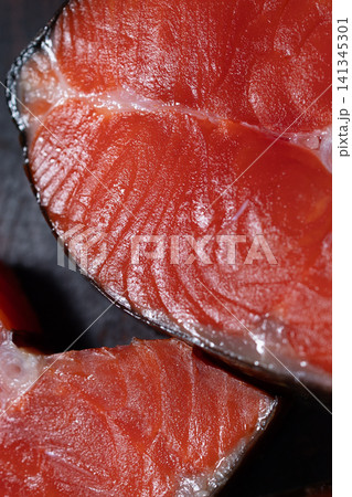 Smoked sockeye salmon steak with glossy red flesh, delicate muscle fibers, thin white connective tissue, rich cured surface, and dark background for dramatic food presentation Smoked sockeye salmon steak with glossy red flesh, delicate muscle fibers, thin white connective tissue, rich cured surface, and dark background for dramatic food presentation 141345301