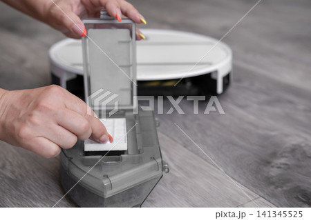 Close up of woman hands replacing or cleaning HEPA filter in robot vacuum dustbin 141345525