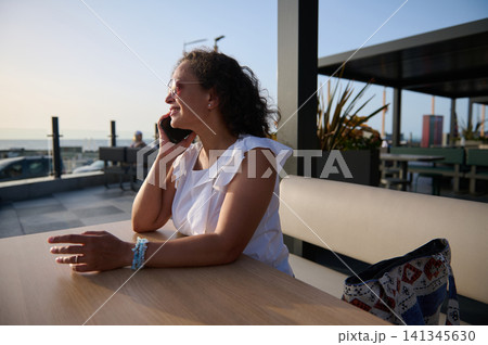 Woman talking on phone at seaside cafe during golden hour Woman talking on phone at seaside cafe during golden hour 141345630