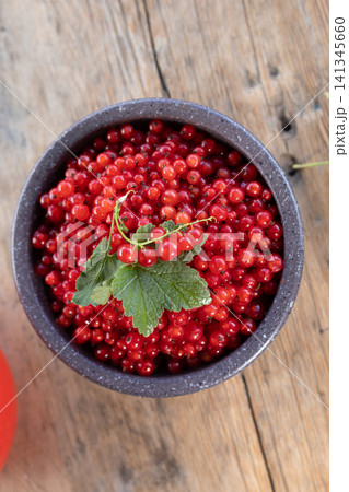 Ripe red currants in rustic ceramic bowl on weathered wooden table with green leaf, glossy clustered berries under soft natural light, fresh seasonal produce for healthy summer food concepts Ripe red currants in rustic ceramic bowl on weathered wooden table with green leaf, glossy clustered berries under soft natural light, fresh seasonal produce for healthy summer food concepts 141345660