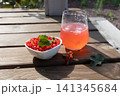 Bowl of fresh red currants with mint leaf and chilled red currant drink on wooden table in sunlight 141345684