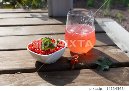 Bowl of fresh red currants with mint leaf and chilled red currant drink on wooden table in sunlight Bowl of fresh red currants with mint leaf and chilled red currant drink on wooden table in sunlight 141345684