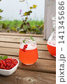 Bright red currant drink in clear glass with berry garnish on rustic wooden table, served beside fresh currants, bowl, pitcher, natural outdoor summer setting, with red, currant, drink, fruit detail 141345686