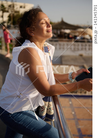 Woman enjoying warm sunlight on a seaside promenade during a relaxed vacation moment Woman enjoying warm sunlight on a seaside promenade during a relaxed vacation moment 141345701