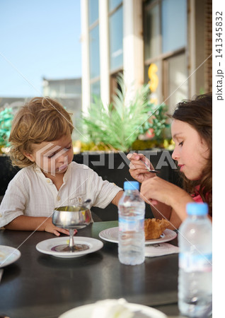 Mother and young child sharing dessert at an outdoor cafe on a sunny day Mother and young child sharing dessert at an outdoor cafe on a sunny day 141345832