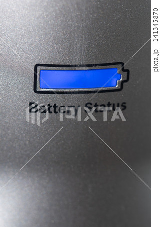 Blue battery indicator illuminated on textured metallic panel with partial status, closeup view showing recessed display, reflective grain, and subtle industrial detailing Blue battery indicator illuminated on textured metallic panel with partial status, closeup view showing recessed display, reflective grain, and subtle industrial detailing 141345870