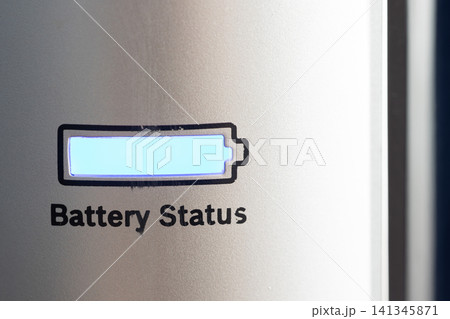 Closeup of illuminated battery icon and partial printed status on metallic device panel with blue glow, textured surface, soft side lighting, and shallow focus, with battery, icon, indicator, status 141345871