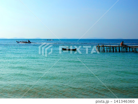 Tropical landscape with turquoise ocean water, wooden pier, and fishing boats Tropical landscape with turquoise ocean water, wooden pier, and fishing boats 141346360