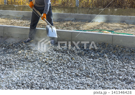 Builder is using shovel to spread gravel on construction site in renovation road Builder is using shovel to spread gravel on construction site in renovation road 141346428