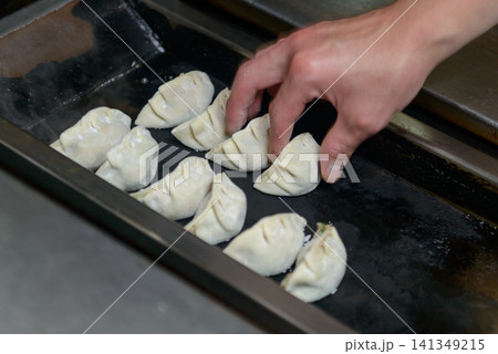 餃子焼き機の鉄板に生の餃子を並べる料理人の手 中華料理店での餃子の調理風景 餃子焼き機の鉄板に生の餃子を並べる料理人の手 中華料理店での餃子の調理風景 141349215