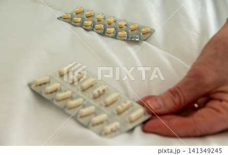 Pill packets on a white bedcover with a hand reaching Pill packets on a white bedcover with a hand reaching 141349245