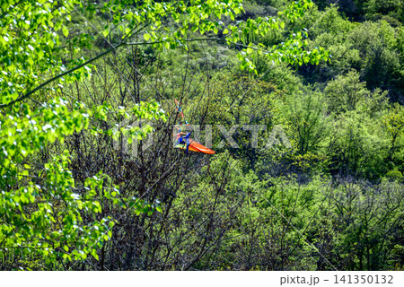 Orange glider above green forest hillside 141350132