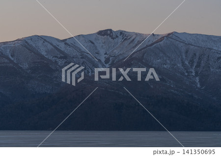 夕暮れの光の帯と山影、静かなカルデラ湖 141350695