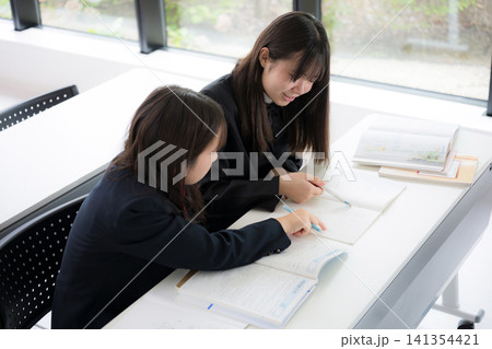 教室で教え合いながら勉強する仲良しの日本人女子中学生と高校生の友達 協力して学ぶ 俯瞰 教室で教え合いながら勉強する仲良しの日本人女子中学生と高校生の友達 協力して学ぶ 俯瞰 141354421