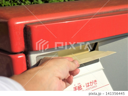 ポストに封筒を投函する瞬間の手元 ポストに封筒を投函する瞬間の手元 141356445