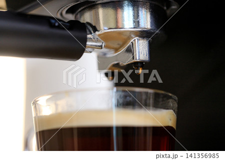 Close-up of an espresso machine brewing freshly extracted black coffee into a clear glass cup, highlighting coffee preparation 141356985