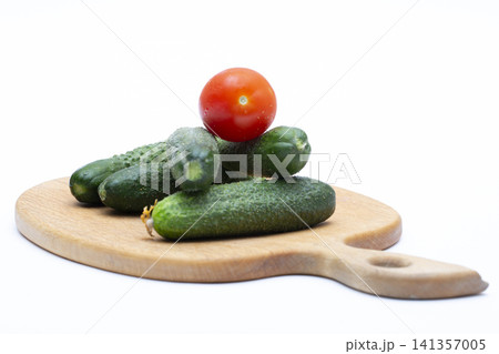 Ripe red tomatoes and cucumbers on a wooden board against a white background 141357005