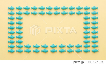 Turquoise plastic fish figurines arranged in rectangular frame pattern against soft yellow background surface with collection identical turquoise Turquoise plastic fish figurines arranged in rectangular frame pattern against soft yellow background surface with collection identical turquoise 141357194
