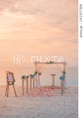 Sunset beach wedding setup in vertical frame, arch and easel on empty shore at dusk. Peach and golden evening light over destination ceremony venue by calm ocean. Warm romantic twilight honeymoon 141357306