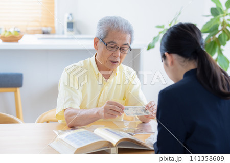 出張買取 自宅で切手や古銭の鑑定をしてもらっているシニア男性 出張買取 自宅で切手や古銭の鑑定をしてもらっているシニア男性 141358609