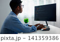 Asian male IT specialist with glasses coding software or programming on desktop computer at home office desk. Concentrated smart student studying computer science online. 141359386