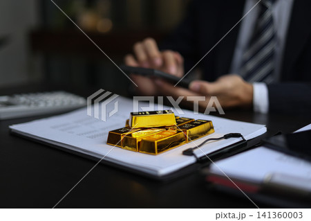 Gold investment. Businessman analyzing financial data with gold bars and calculator on desk Gold investment. Businessman analyzing financial data with gold bars and calculator on desk 141360003