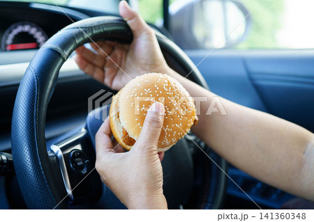Asian woman driver hold and eat hamburger food in car. Asian woman driver hold and eat hamburger food in car. 141360348