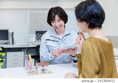 建築模型を見ながら打ち合わせする作業服の女性 建築模型を見ながら打ち合わせする作業服の女性 141360411