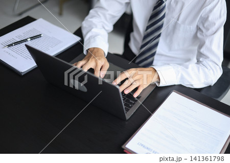 Professional lawyer reviewing a legal business contract while working on laptop in modern office. 141361798