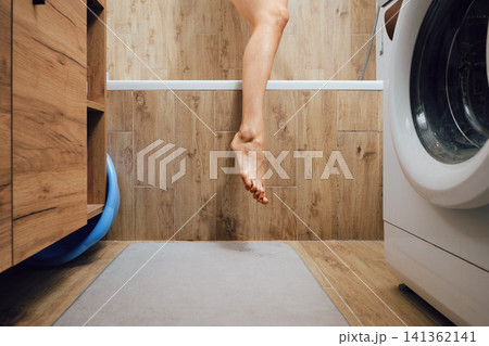 Female foot hanging over edge of bathtub in modern bathroom 141362141