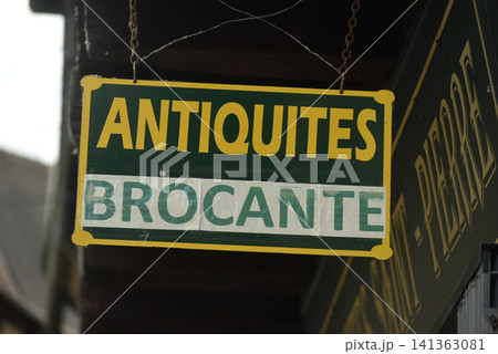 Street view of a sign reading "Antiquites Brocante" on a building, representing an antique shop and second hand market atmosphere in an urban environment. Street view of a sign reading "Antiquites Brocante" on a building, representing an antique shop and second hand market atmosphere in an urban environment. 141363081