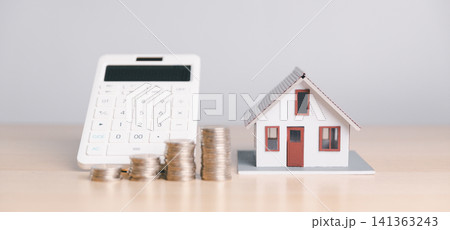 House model with calculator and coin stacks on wooden table, representing mortgage calculation, home loan budget, property tax, real estate cost, and financial planning. 141363243