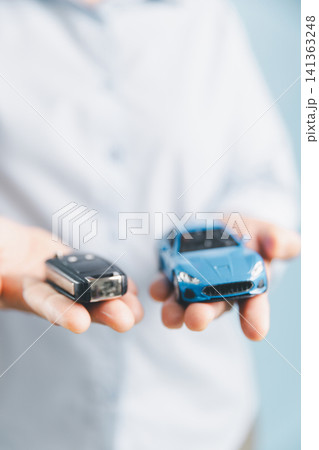 Person holding a car key and blue toy car, representing car delivery, vehicle ownership, financing completion, insurance, and the final step of car purchase. 141363248