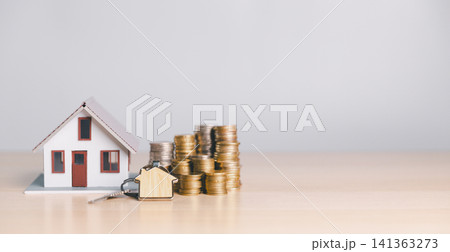 Small house model with home key and stacked coins on wooden table, representing home buying, mortgage savings, property ownership, down payment, and real estate finance. 141363273