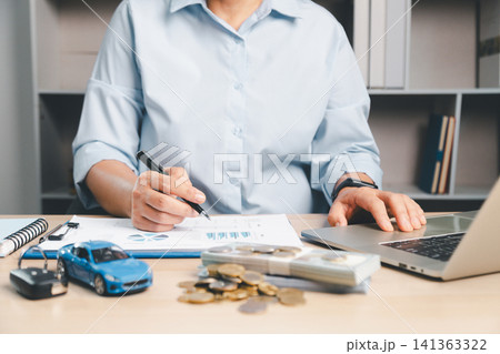 Business professional reviewing financial documents with laptop, toy car, cash, coins, and car key, representing car finance, auto loan planning, vehicle ownership, and transportation cost management. Business professional reviewing financial documents with laptop, toy car, cash, coins, and car key, representing car finance, auto loan planning, vehicle ownership, and transportation cost management. 141363322