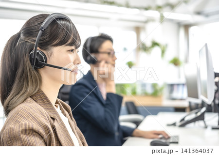 オフィスでヘッドセットを使って働く男女の会社員 オフィスでヘッドセットを使って働く男女の会社員 141364037