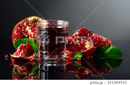 Pomegranate and a glass of ruby-red juice on a black reflective background. Pomegranate and a glass of ruby-red juice on a black reflective background. 141364555