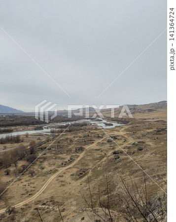 Aerial view of winding river through dry valley with scattered trees and hills. Aerial view of winding river through dry valley with scattered trees and hills. 141364724
