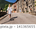 Young woman in white dress walking along historic stone village street in Catalonia, enjoying peaceful summer travel 141365655