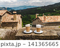 Two cappuccino cups on stone terrace overlooking peaceful mountain village 141365665