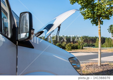 White camper van on a highway rest area with an open hood parked on a roadside for an engine check, indicating trouble or maintenance during a road trip. Copy space White camper van on a highway rest area with an open hood parked on a roadside for an engine check, indicating trouble or maintenance during a road trip. Copy space 141366070