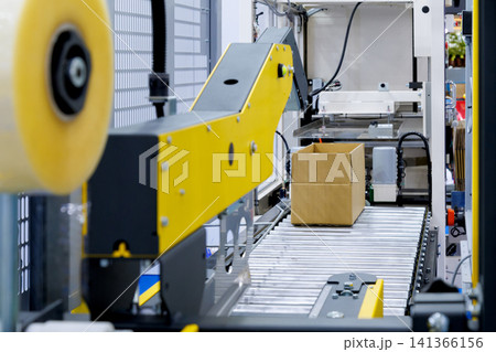 brown cardboard box on roller of conveyor belt at automatic carton sealing machine. Industrial product packaging, logistics, and e-commerce fulfillment factory automation concept brown cardboard box on roller of conveyor belt at automatic carton sealing machine. Industrial product packaging, logistics, and e-commerce fulfillment factory automation concept 141366156