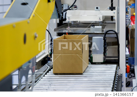 brown cardboard box on roller of conveyor belt at automatic carton sealing machine. Industrial product packaging, logistics, and e-commerce fulfillment factory automation concept brown cardboard box on roller of conveyor belt at automatic carton sealing machine. Industrial product packaging, logistics, and e-commerce fulfillment factory automation concept 141366157