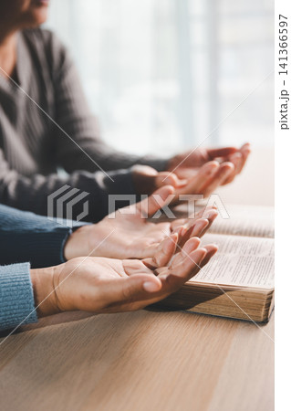 Open hands praying beside open Bible on wooden table with soft sunlight, representing Christian worship, surrender, gratitude, hope and spiritual devotion. Open hands praying beside open Bible on wooden table with soft sunlight, representing Christian worship, surrender, gratitude, hope and spiritual devotion. 141366597
