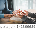 Open hands praying over Bible on wooden table with soft warm light, representing Christian faith, worship, devotion, gratitude, hope and spiritual peace. 141366689