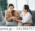 Middle aged Asian woman comforting sad adult daughter by holding hands on sofa at home, concept of emotional support, family care, empathy, counseling, and trust. 141366757