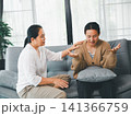 Asian mother listening and comforting adult daughter during serious conversation on sofa at home, concept of family counseling, emotional support, trust, and mental wellness. 141366759