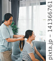 Asian mother tying adult daughter hair into ponytail at home, concept of family care, grooming, haircare routine, personal care, bonding, and domestic lifestyle. 141366761