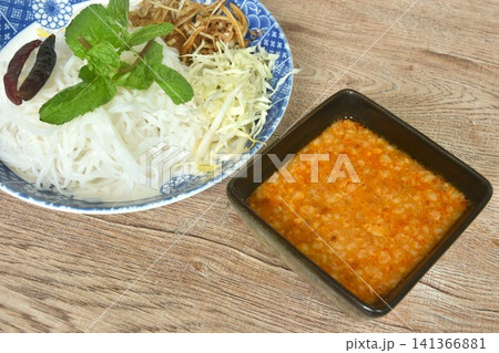 rice noodles topping fried chili and fresh vegetable on plate with sweet coconut milk mashed bean curry sauce in bowl rice noodles topping fried chili and fresh vegetable on plate with sweet coconut milk mashed bean curry sauce in bowl 141366881